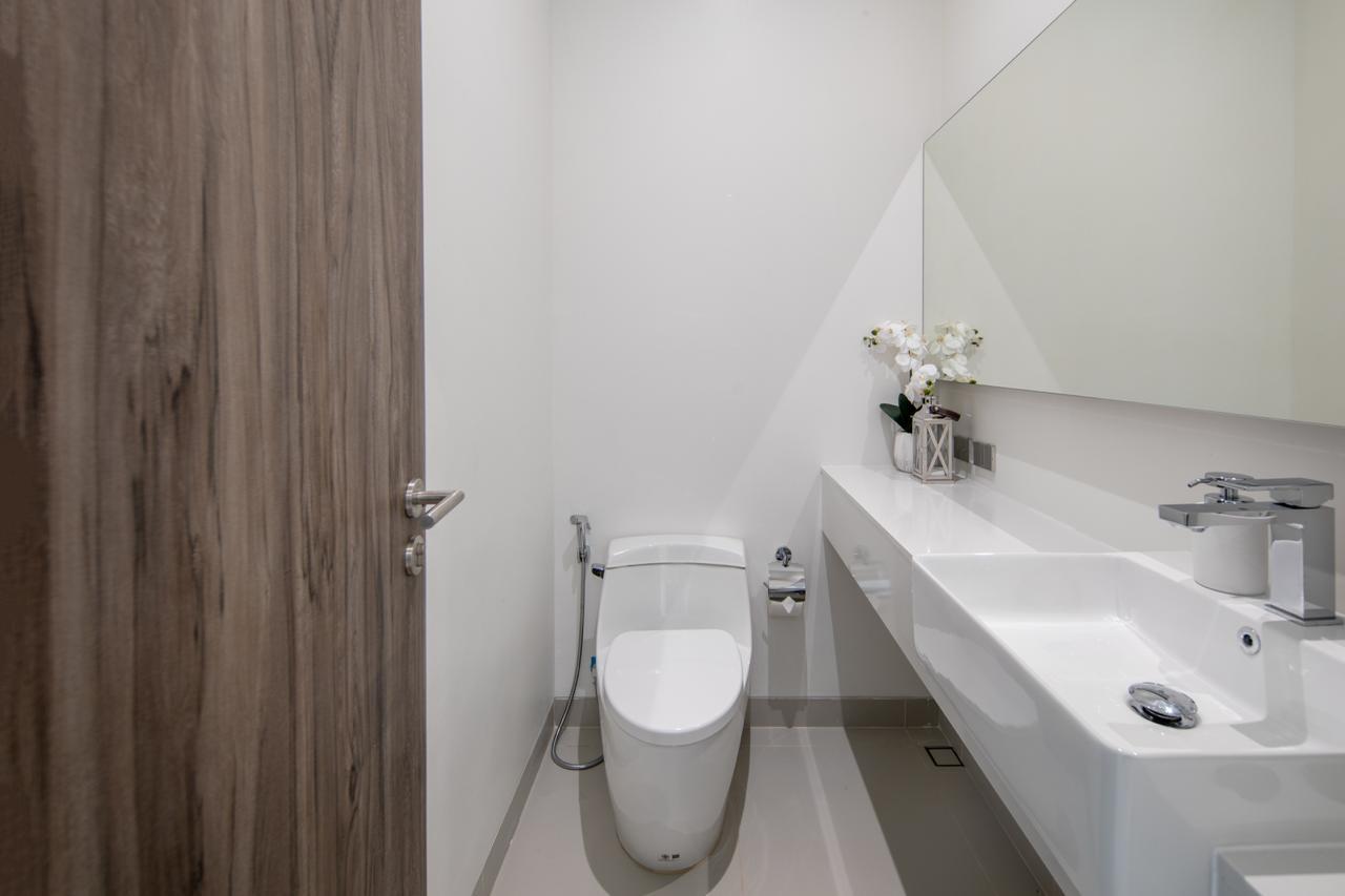Small modern bathroom with a white toilet and a long white countertop sink, mirror, and flower vase.