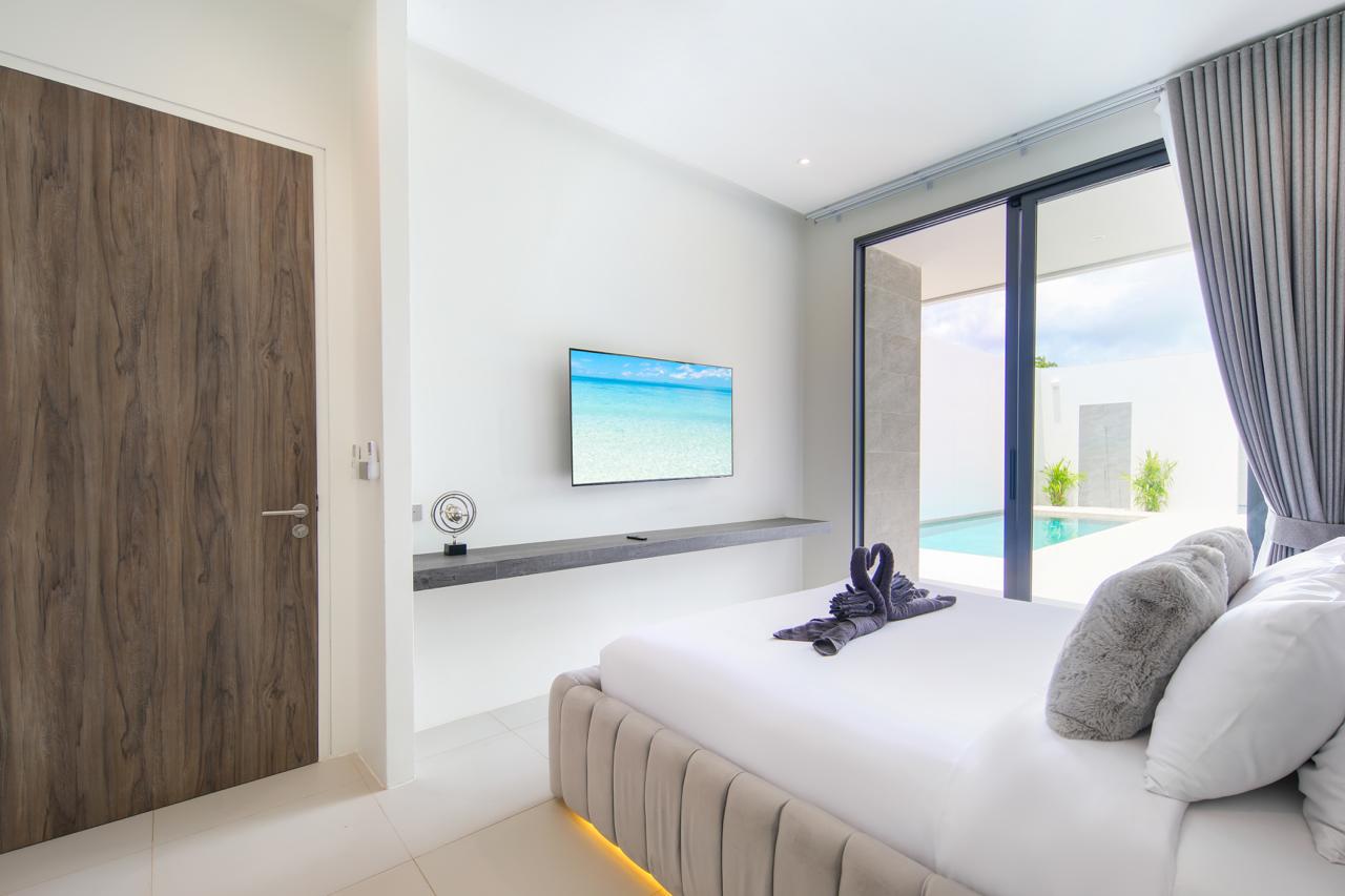 Minimalist hotel bedroom with a large bed, gray throw pillows, and sliding glass doors to a poolside view outside home-like balcony area.