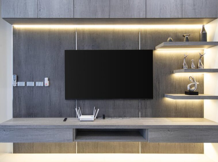 Modern gray wall unit with a large flat-screen TV, a floating console, and lit shelves displaying metallic sculptures.