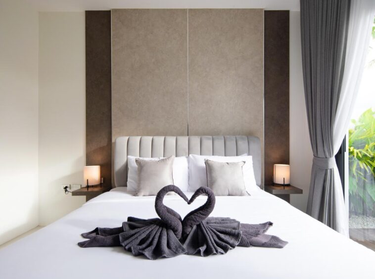Bed with white linens and a decorative pair of towel swans forming a heart at the center of the mattress.