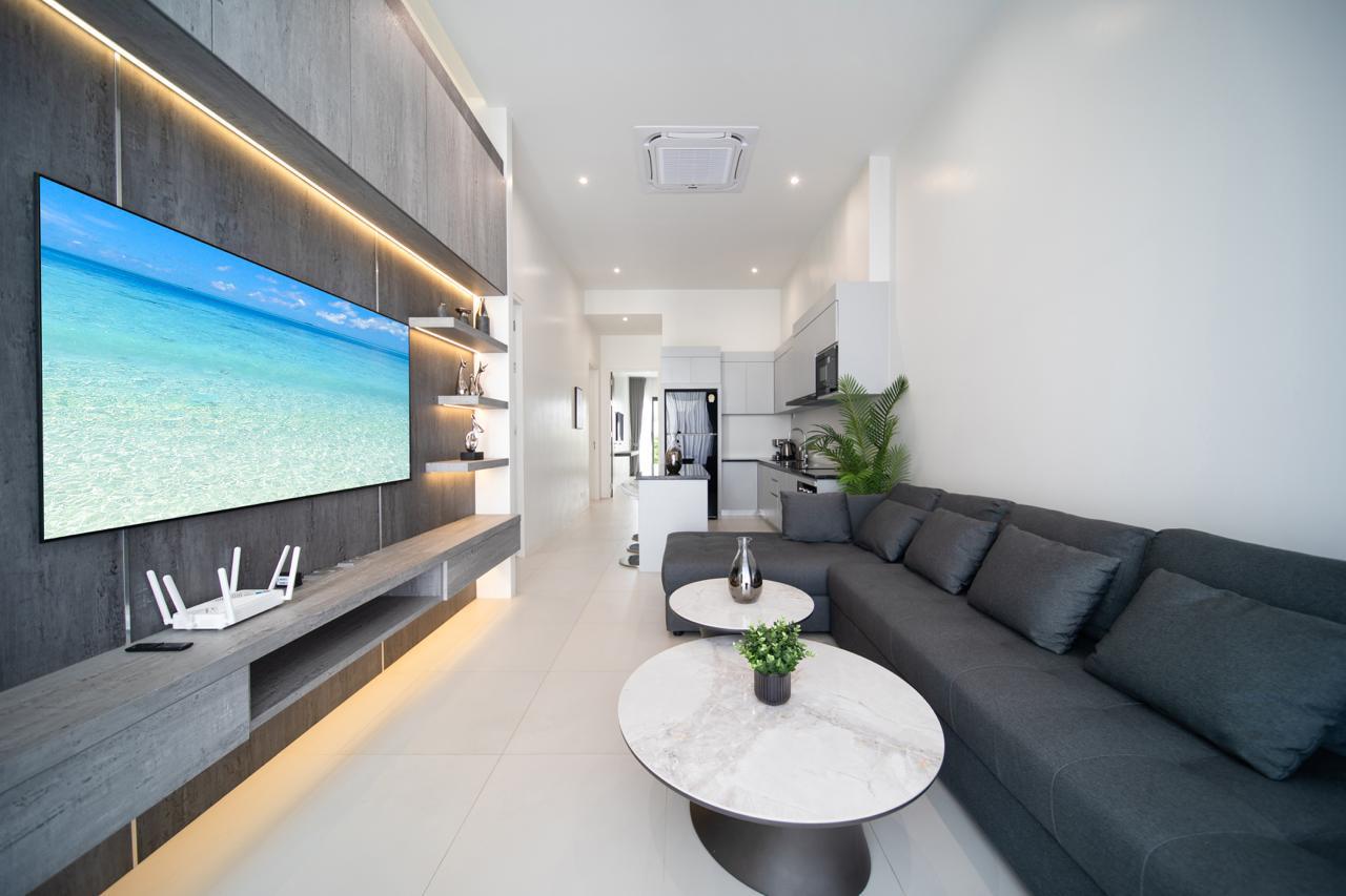 Open-concept living area with a dark gray sectional, two round marble coffee tables, and a wall-mounted jungle beach TV wall; kitchen in the background.
