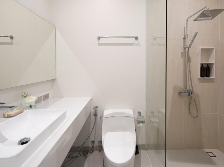 Modern white bathroom with a long vanity, wall mirror, toilet, and glass-enclosed shower.