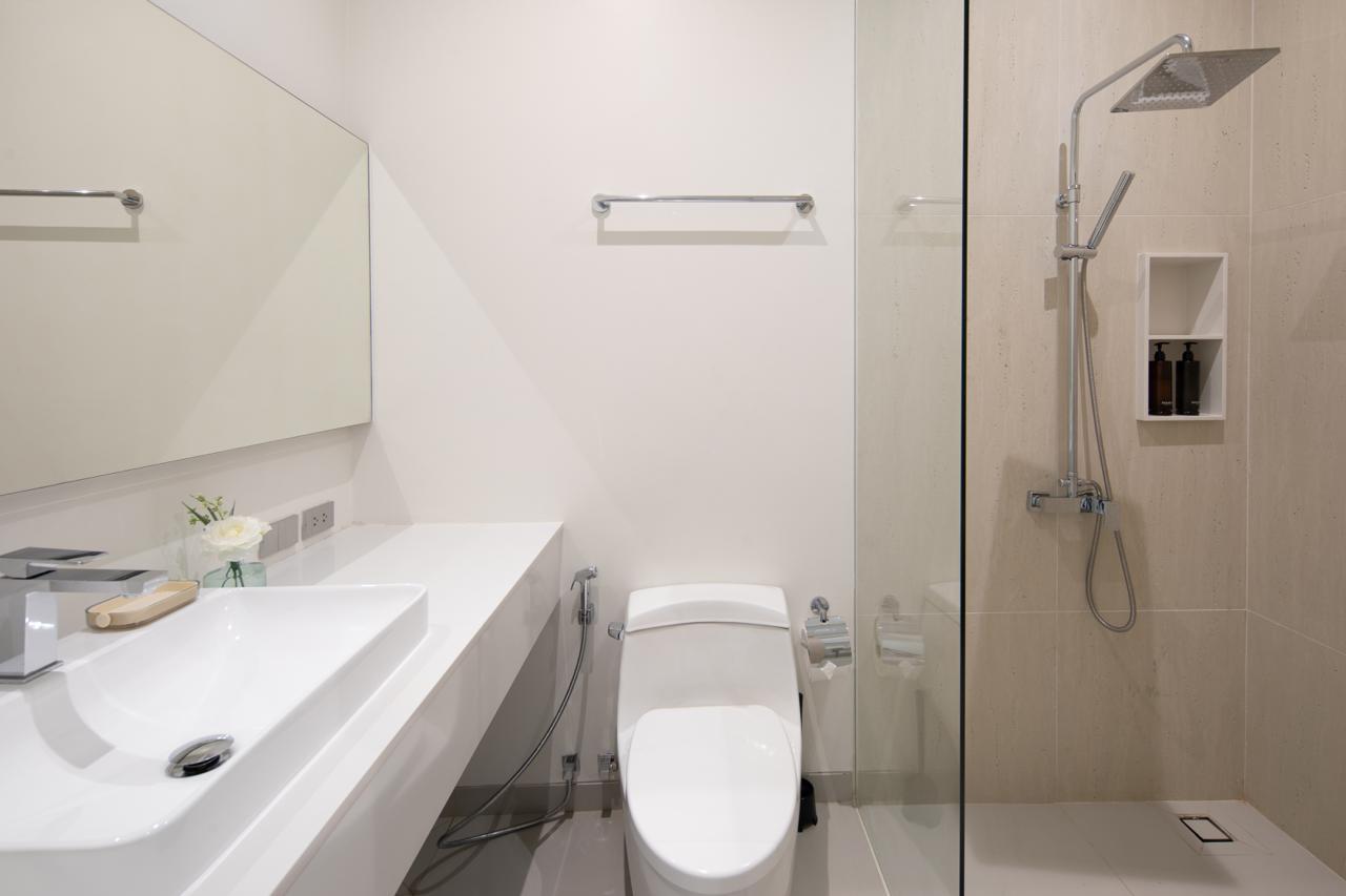 Modern white bathroom with a long vanity, wall mirror, toilet, and glass-enclosed shower.