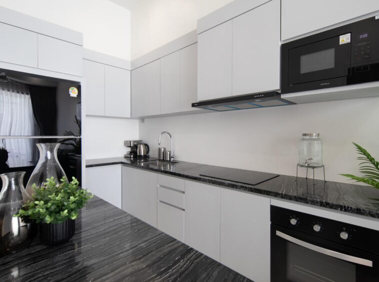 Modern gray kitchen with black marble countertops, built-in oven and microwave, and a sink along the counter. (Informative)