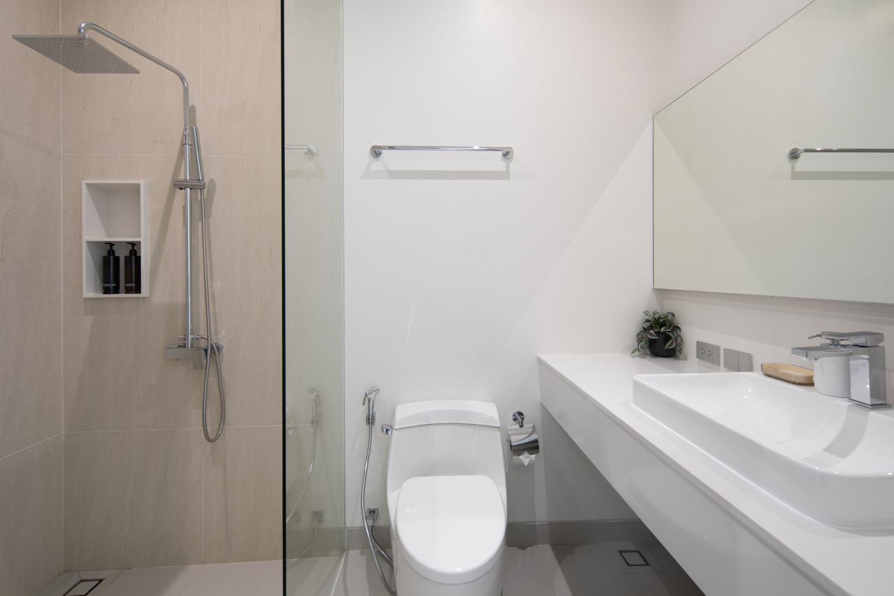Modern bathroom with a glass shower enclosure, wall-mounted sink, and toilet in a bright, minimal design.
