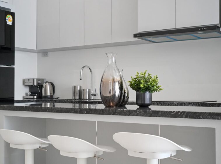 Modern kitchen island with a black marble countertop, three white bar stools, and a glass carafe center stage.