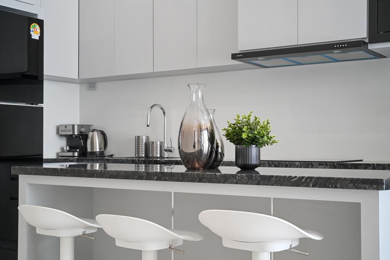Modern kitchen island with a black marble countertop, three white bar stools, and a glass carafe center stage.