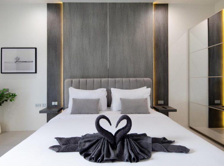 Modern hotel bedroom with a white bed, gray tufted headboard, two white pillows and two gray throw pillows; towel swans on the bed.