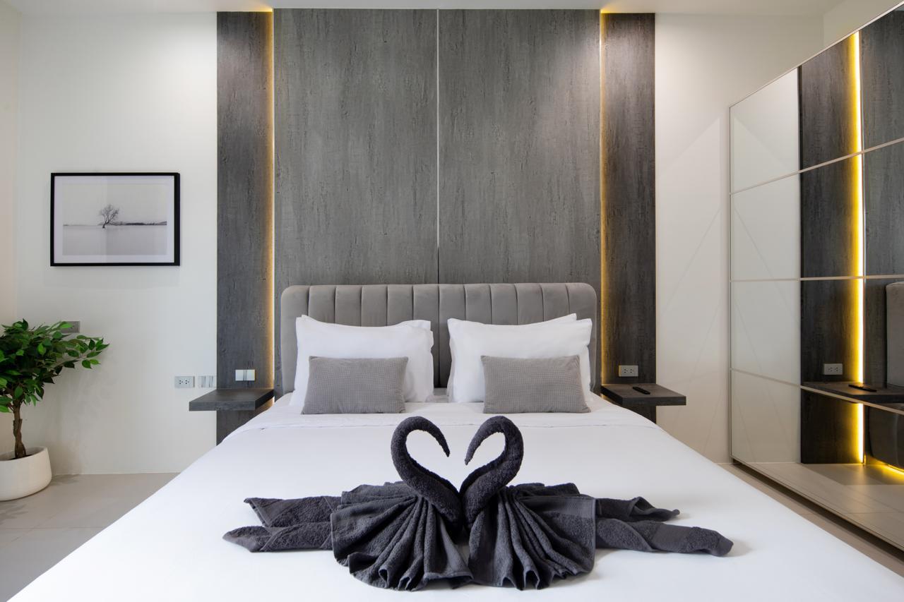 Modern hotel bedroom with a white bed, gray tufted headboard, two white pillows and two gray throw pillows; towel swans on the bed.