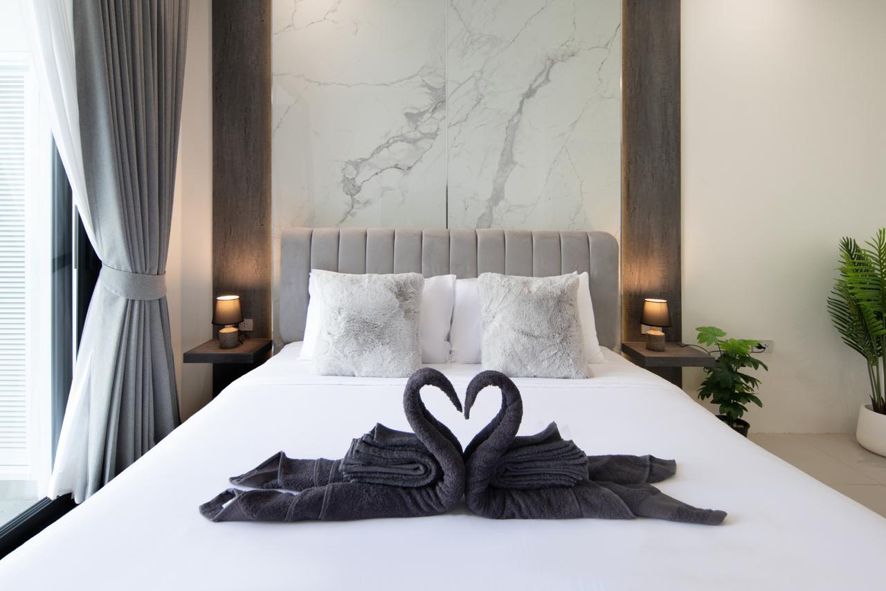 Luxurious bedroom with a tufted gray headboard, marble wall panels, and swan-shaped towels on a white duvet.
