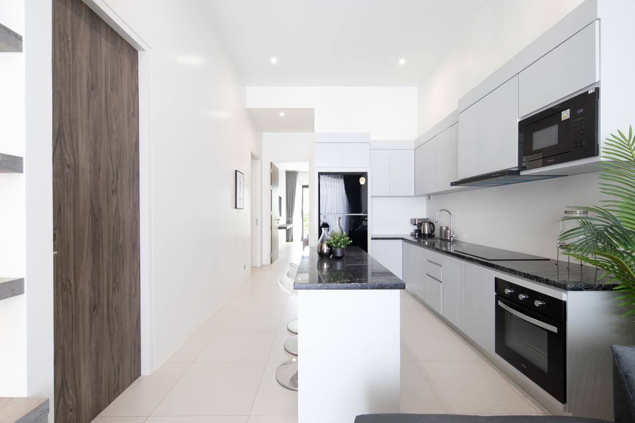 Bright modern kitchen with white walls, grey cabinets, black countertops, and stainless-steel appliances along a long counter.