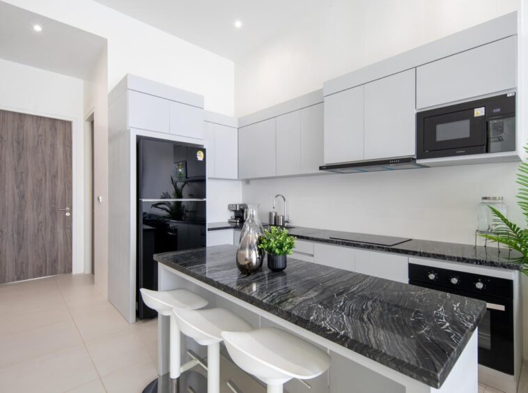 Modern white kitchen with a black marble island, bar stools, and stainless appliances.