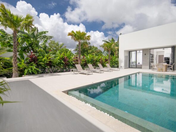 Rectangular pool on a white deck with beige lounge chairs and tropical plants nearby.