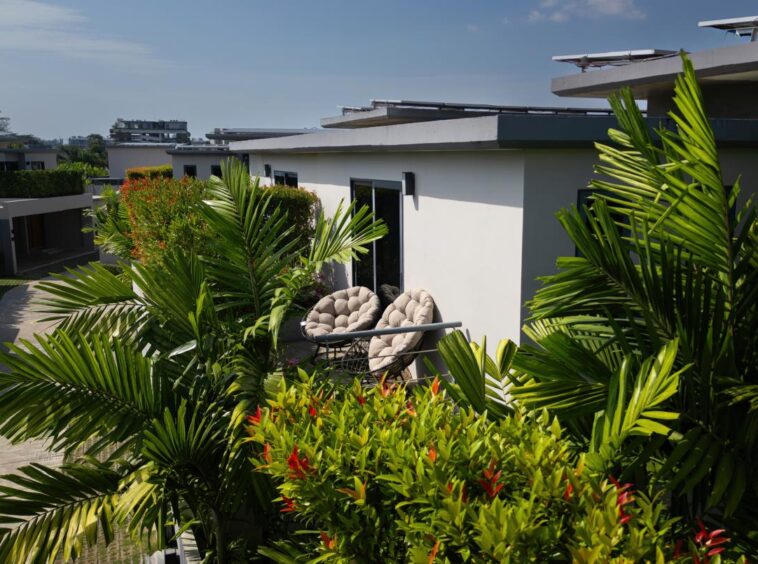 Balcony area of a modern white building with cushioned round chairs amid lush tropical plants and greenery.