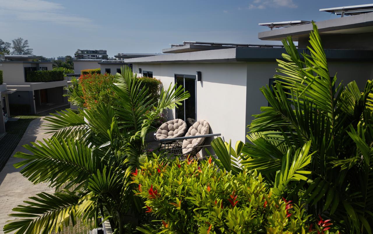 Balcony area of a modern white building with cushioned round chairs amid lush tropical plants and greenery.