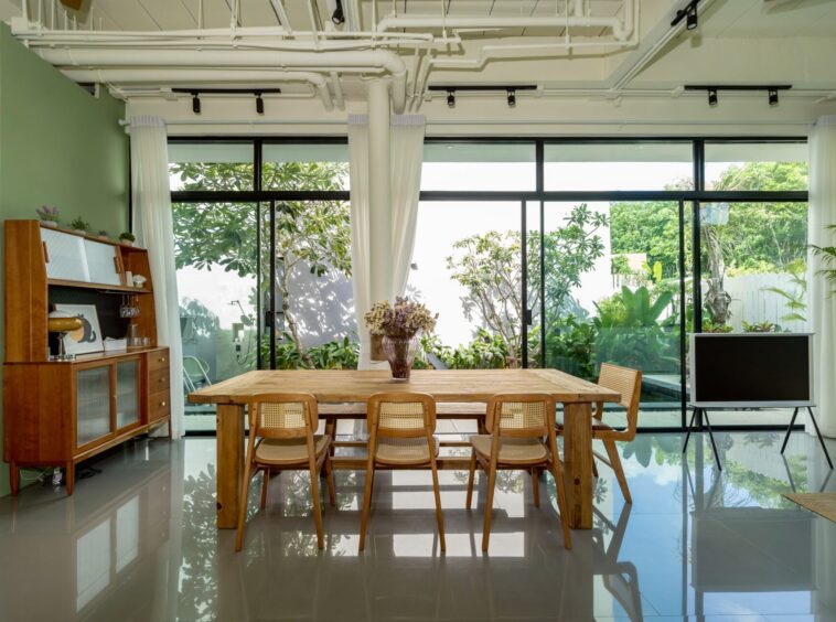 Open-plan dining room with a wooden table and chairs, large glass doors showing a lush garden outside.