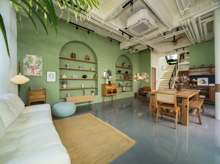 Open loft-style living area with green accent wall, built-in shelves, and a large wooden dining table in the foreground