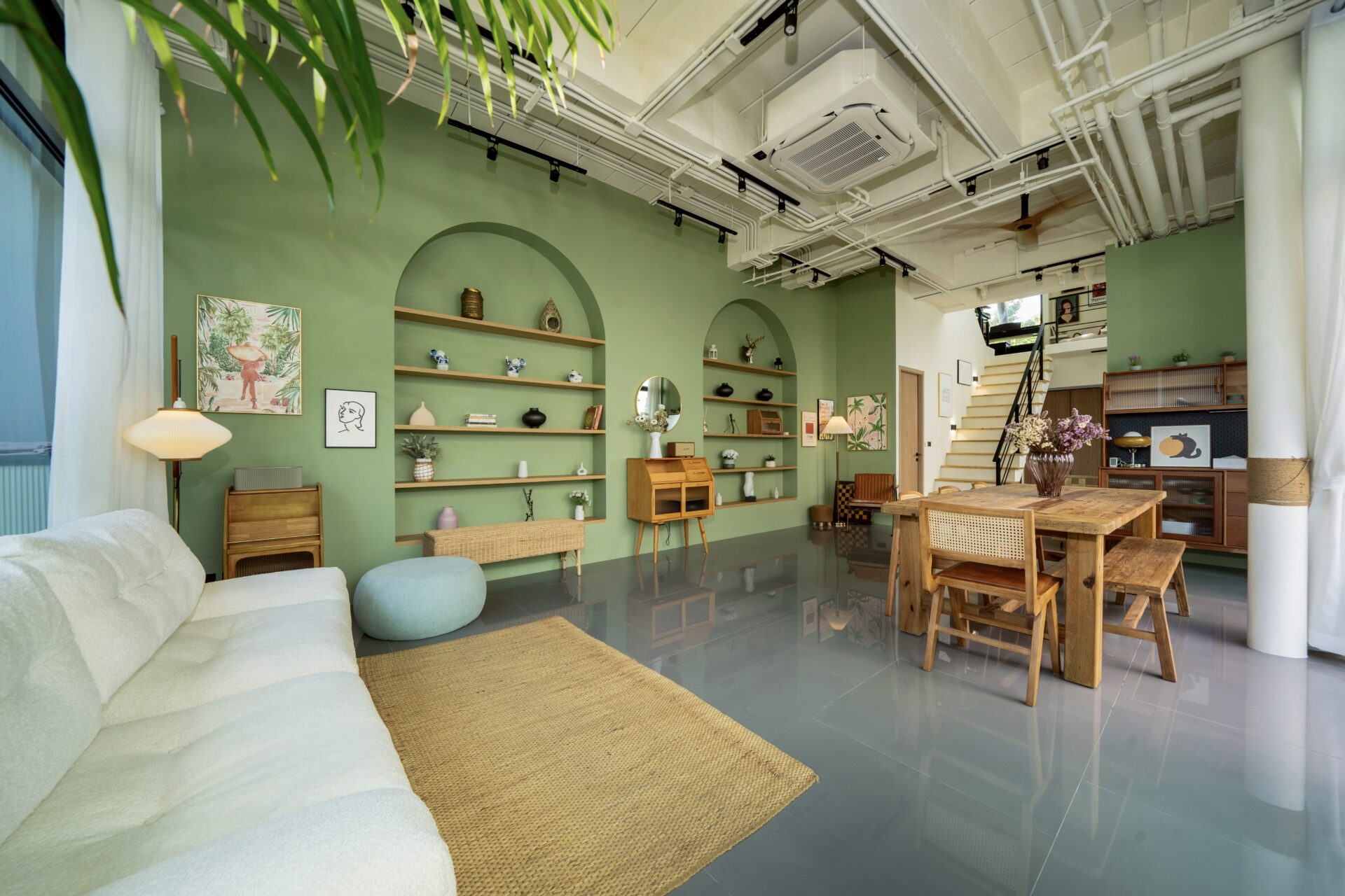 Open loft-style living area with green accent wall, built-in shelves, and a large wooden dining table in the foreground