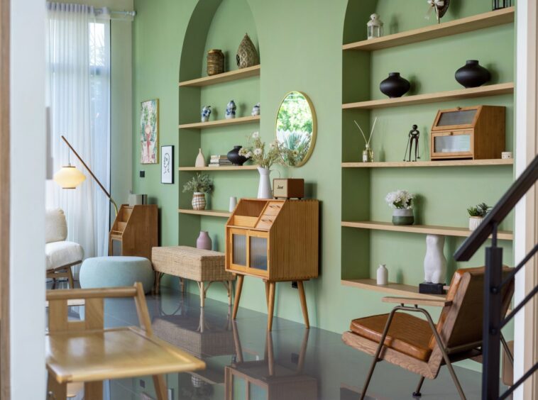 Cozy living room with green walls, built-in wooden shelves, and mid-century furniture including a wicker cabinet and chairs.