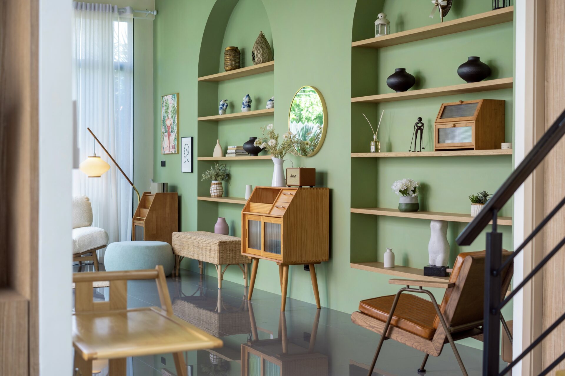 Cozy living room with green walls, built-in wooden shelves, and mid-century furniture including a wicker cabinet and chairs.