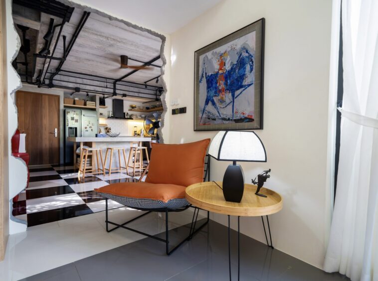 Open-plan living area with orange-cushioned chair and round wooden table facing a large abstract painting on the wall