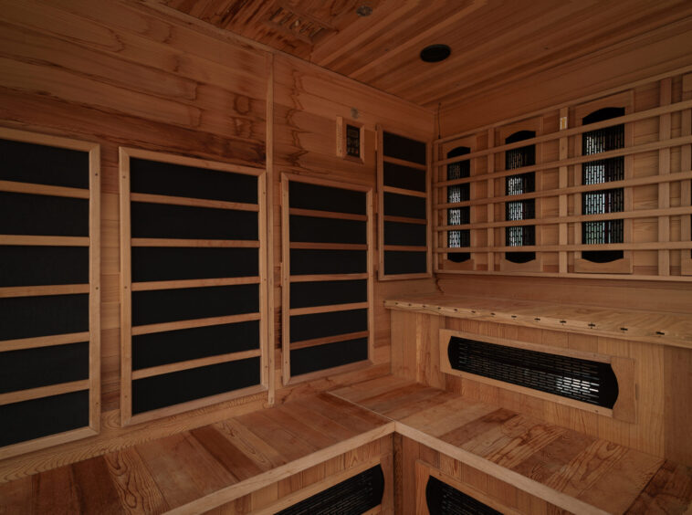 Wood-paneled sauna interior with tiered benches and a heater vent along the wall, creating a warm, relaxing space.