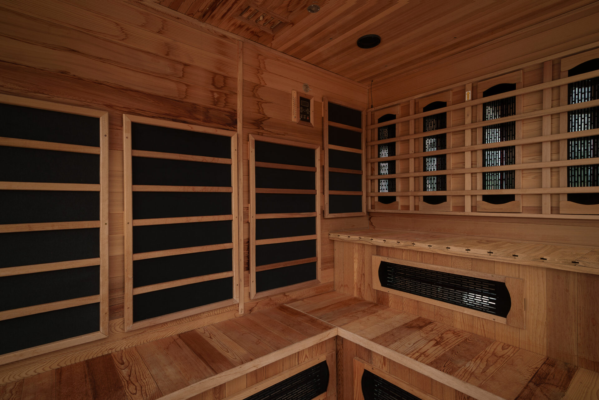 Wood-paneled sauna interior with tiered benches and a heater vent along the wall, creating a warm, relaxing space.