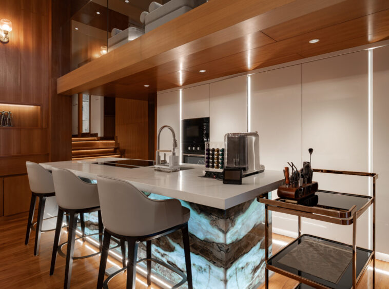 Modern kitchen with a marble island, warm wood paneling, and white bar seating along the island edge.