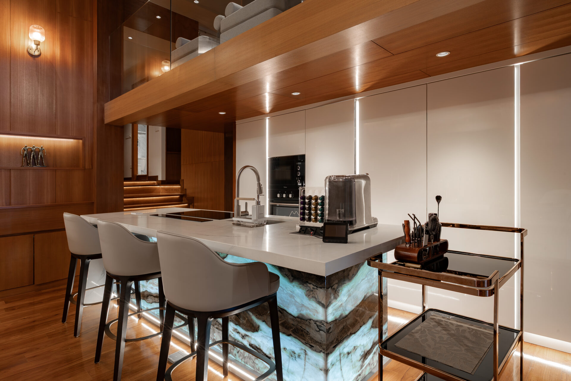 Modern kitchen with a marble island, warm wood paneling, and white bar seating along the island edge.