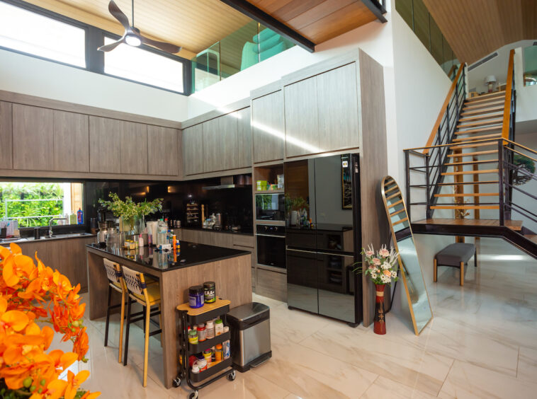 Modern open-plan kitchen with a central island, dark wood cabinetry, and a black refrigerator; staircase on the right.