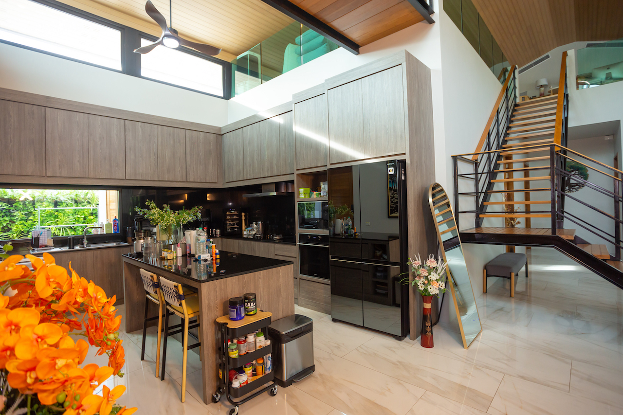 Modern open-plan kitchen with a central island, dark wood cabinetry, and a black refrigerator; staircase on the right.