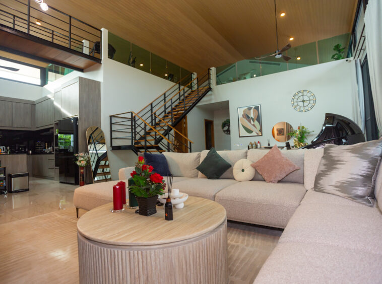 Open-plan living room with a beige sectional sofa, round wooden coffee table, and a grand piano against the wall in a modern home interior