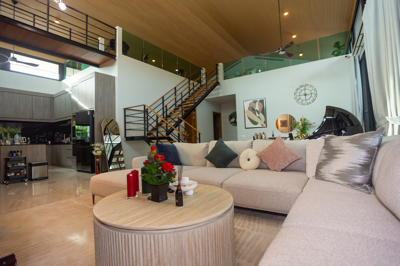 Open-plan living room with a beige sectional sofa, round wooden coffee table, and a grand piano against the wall in a modern home interior