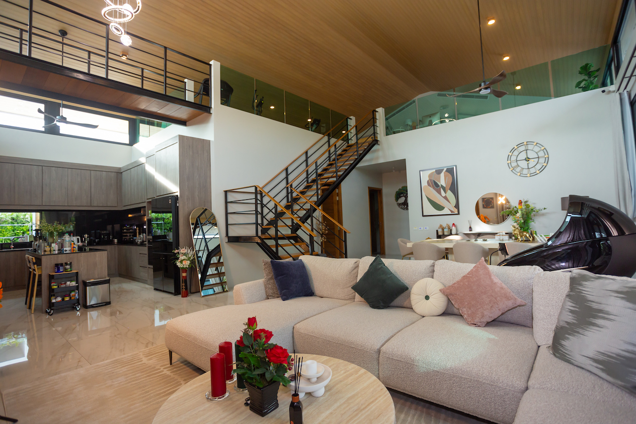 Open-plan living area with a large beige sectional, round coffee table, decorative cushions, and a metal staircase to a mezzanine.