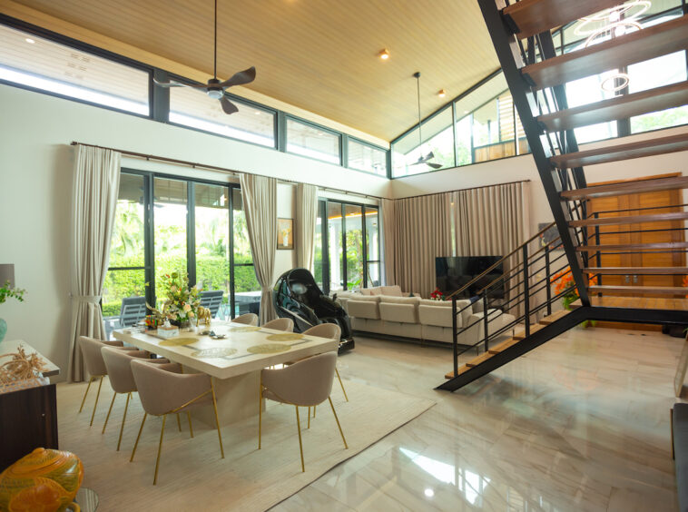 Open-plan living and dining area with a large glass door patio, beige dining table and eight chairs, and a black metal staircase to the right.