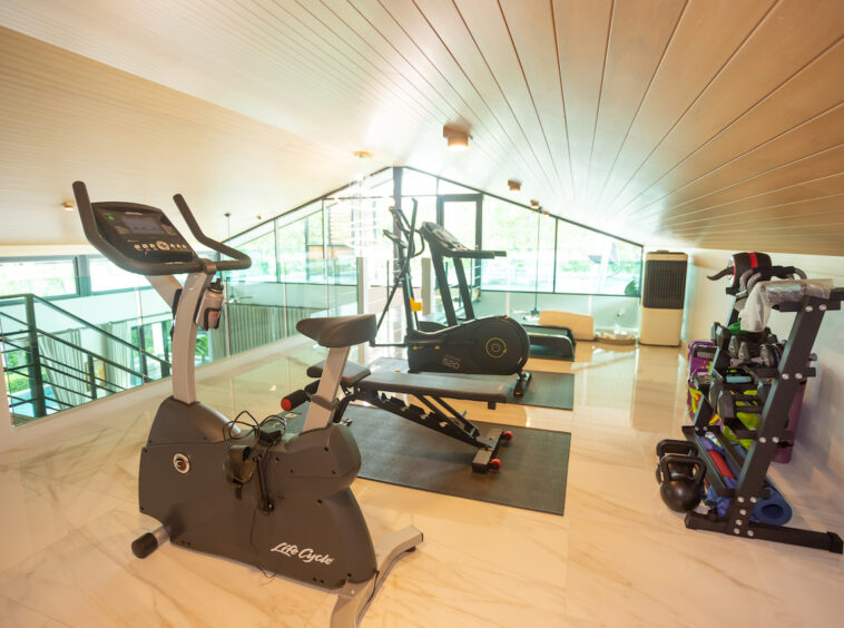 Modern home gym with a stationary bike, a treadmill, and a weight rack under a sloped wooden ceiling on marble floors