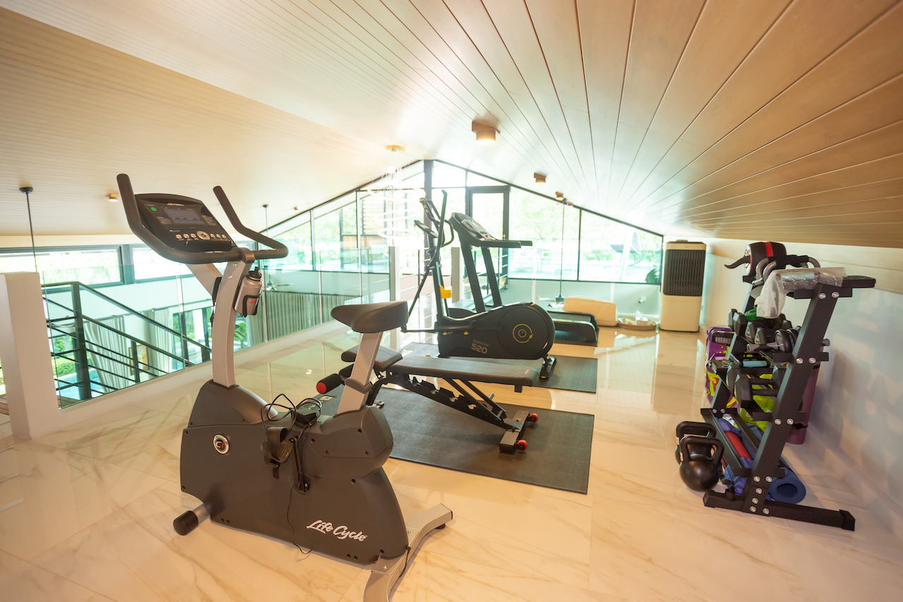 Modern home gym with a stationary bike, a treadmill, and a weight rack under a sloped wooden ceiling on marble floors
