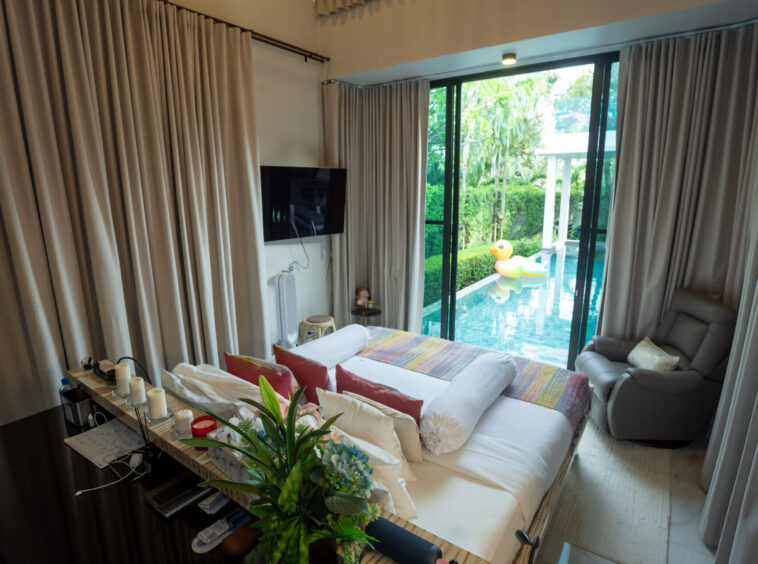 Bedroom with a view: bed facing sliding glass doors to a pool area and a rubber duck float outside, beige curtains on sides.