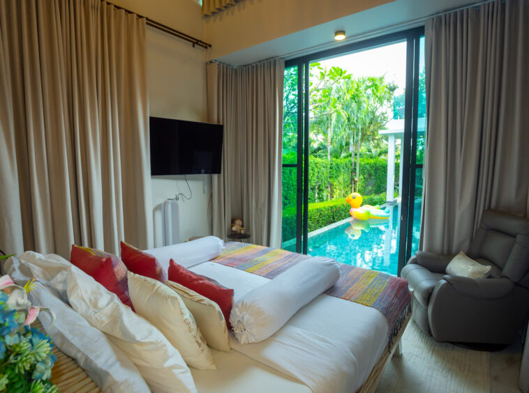 Bedroom with a king bed and colorful pillows, large glass doors reveal a pool with a yellow inflatable duck outside.
