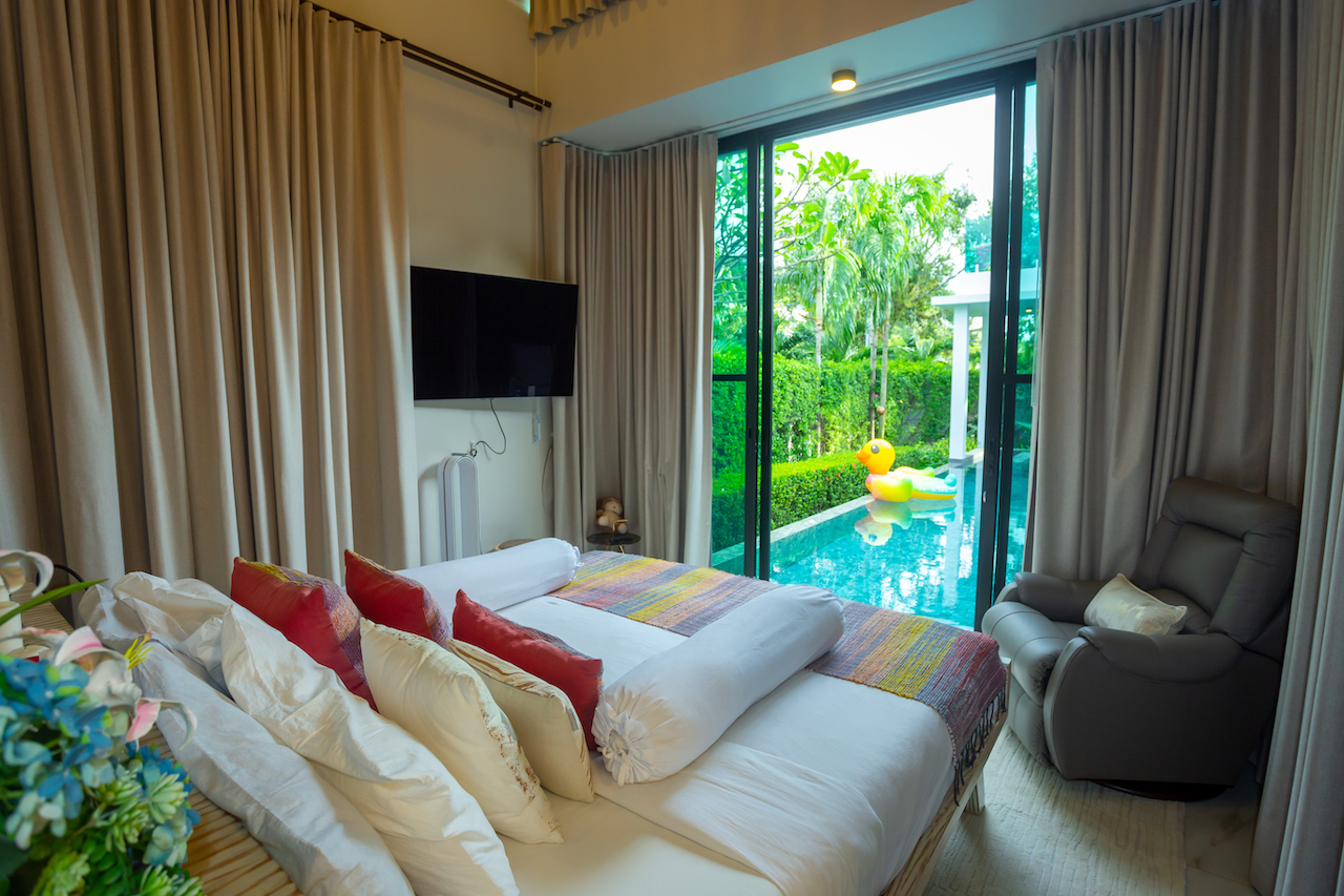 Bedroom with a king bed and colorful pillows, large glass doors reveal a pool with a yellow inflatable duck outside.
