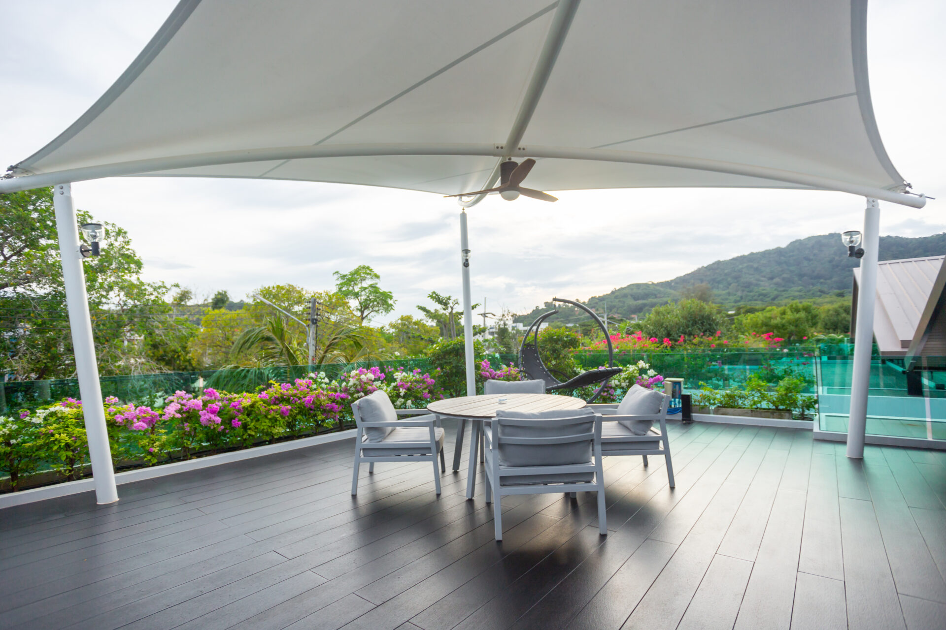 Outdoor patio with a round table and chairs under a large white canopy, lush garden flowers in the background and hills in the distance.