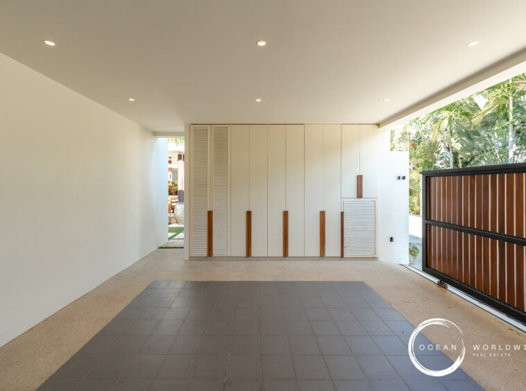 Modern covered outdoor hallway with white storage cabinets and vertical wooden handles, opening to a tropical garden."