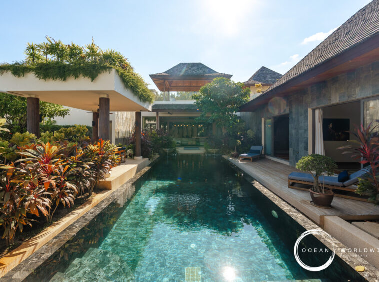 Poolside at a tropical resort with clear blue water, lush plants, and sunlit lounge areas; Ocean Worldwide logo in the corner.