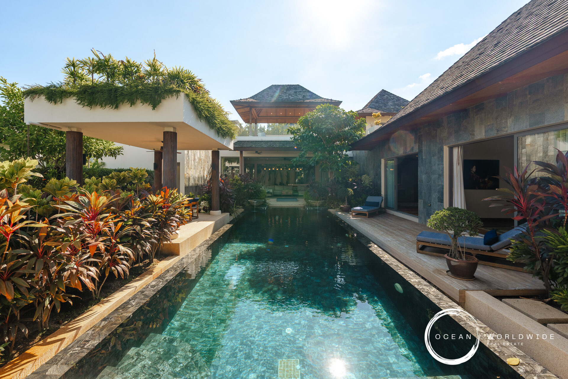 Poolside at a tropical resort with clear blue water, lush plants, and sunlit lounge areas; Ocean Worldwide logo in the corner.