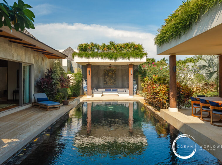 Luxurious villa courtyard with a rectangular pool, greenery, and a shaded seating area under a canopy between stone walls.