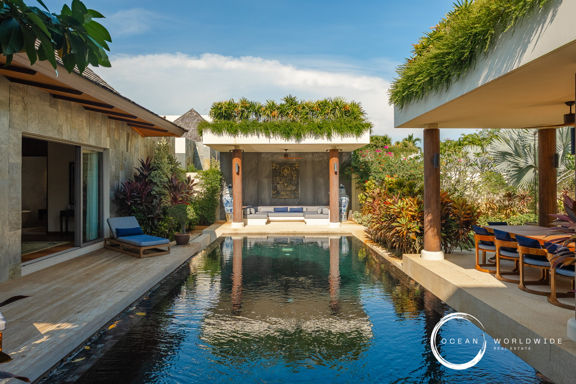 Luxurious villa courtyard with a rectangular pool, greenery, and a shaded seating area under a canopy between stone walls.