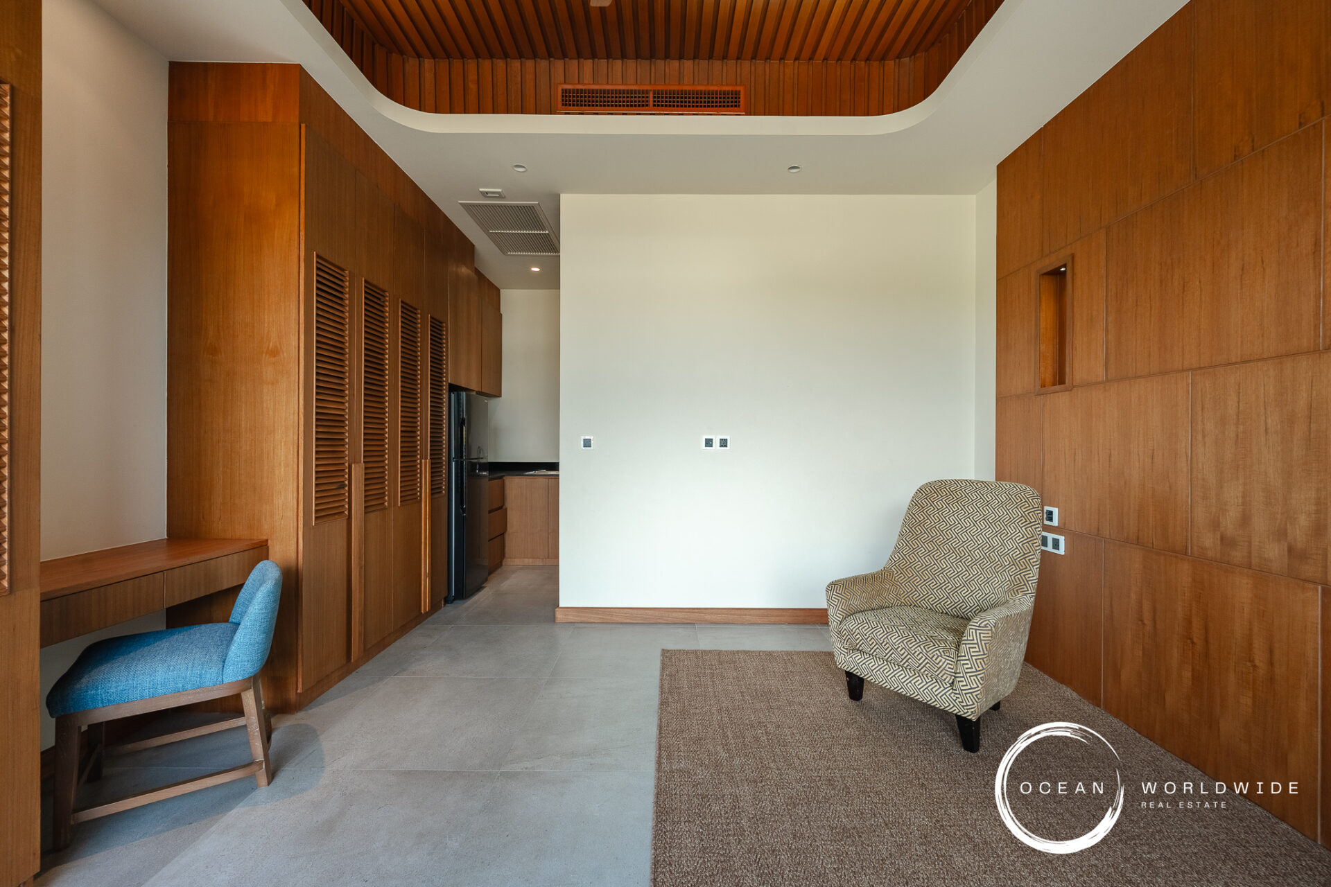 Contemporary living area with floor-to-ceiling wood panels, a blue upholstered desk chair, and a patterned armchair in the foreground.
