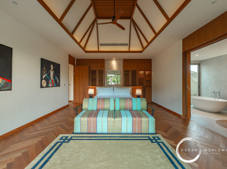 Luxurious hotel bedroom with a vaulted wooden ceiling, king bed, matching nightstands, and turquoise striped sofas facing each other at the foot of the bed.