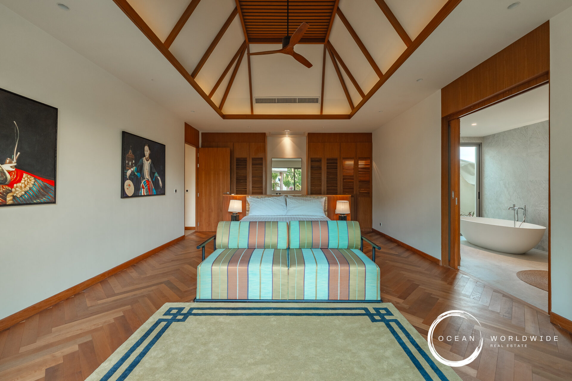 Luxurious hotel bedroom with a vaulted wooden ceiling, king bed, matching nightstands, and turquoise striped sofas facing each other at the foot of the bed.