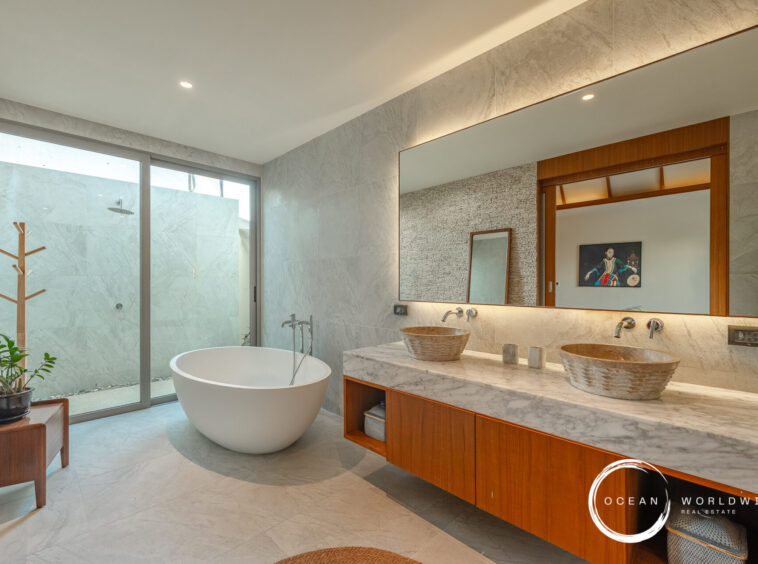 Modern marble bathroom with a freestanding oval bathtub, double vessel sinks, and a large backlit mirror above a wooden vanity.
